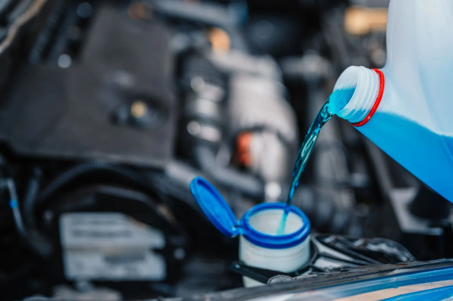Blue fluid being poured from a jug into an engine reservoir