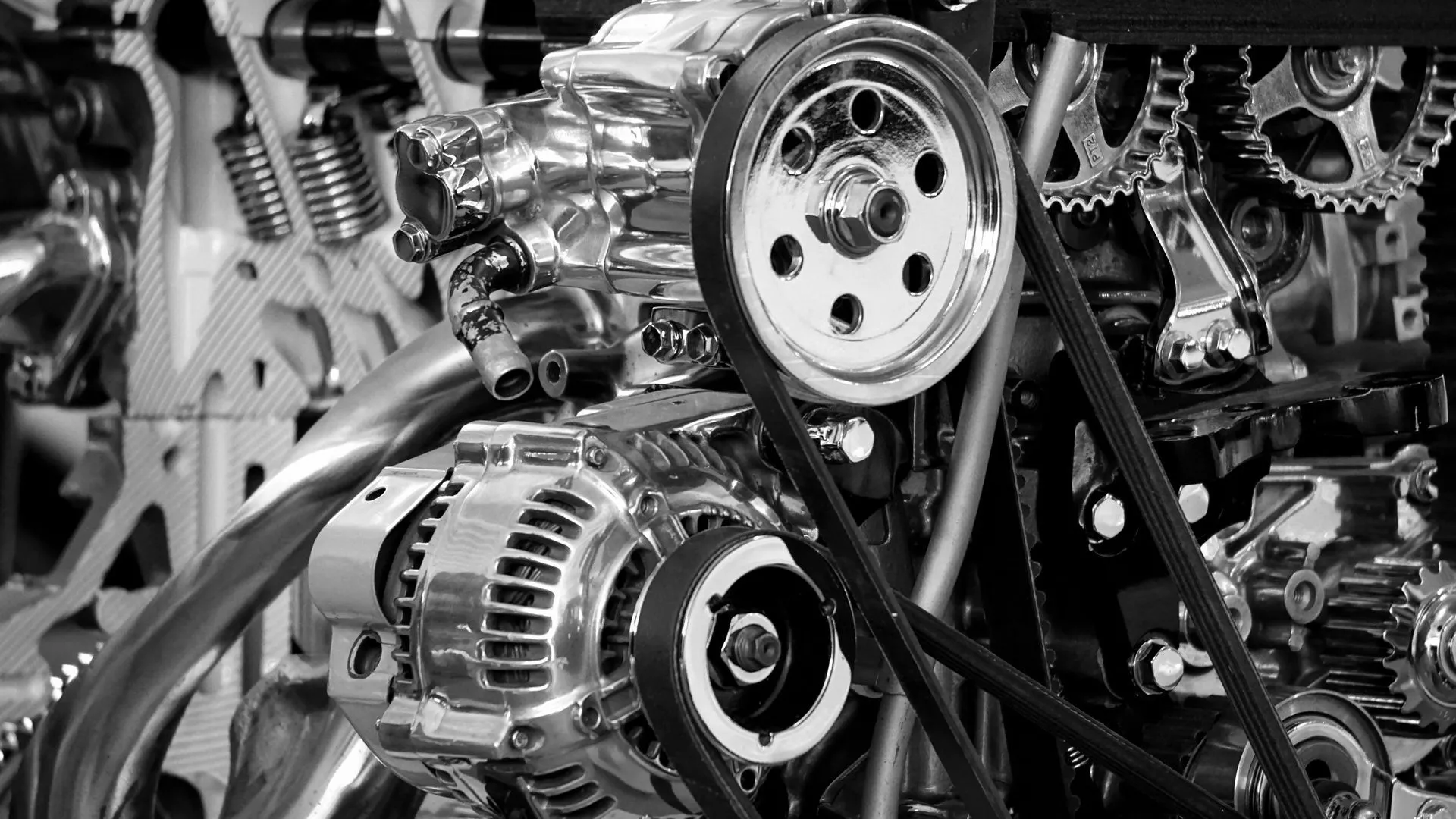 Black-and-white close-up of an engine's drive belts, pulleys and alternator