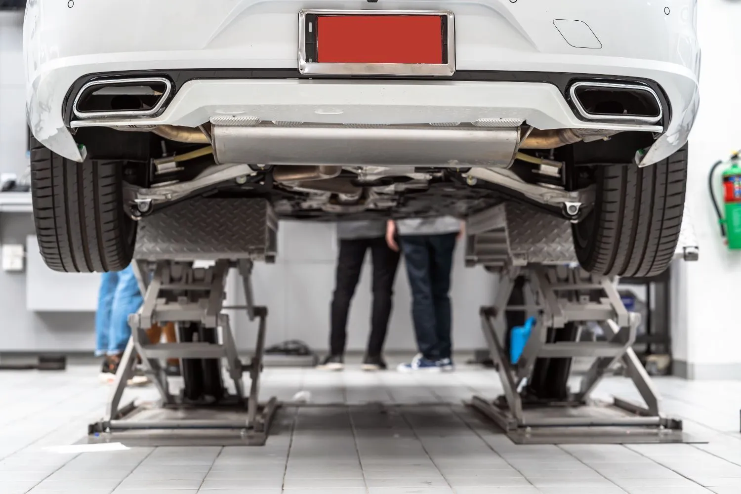 Rear of a white car raised on a lift, showing its dual exhaust tips and underbody